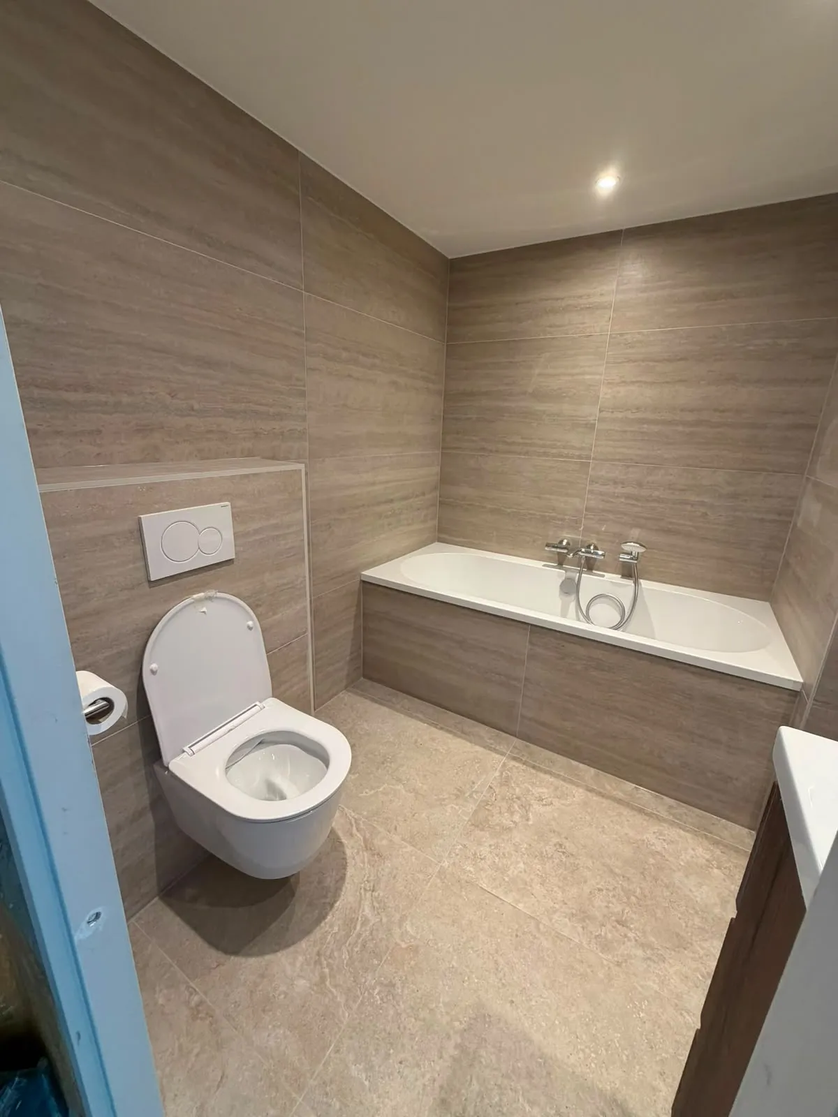 Badkamer met ligbad en hangtoilet in travertinlook tegels