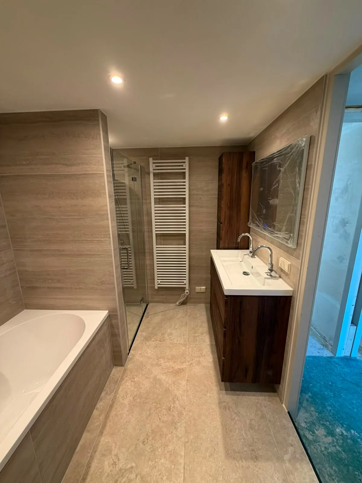 Badkamer met glazen douchecabine, handdoekradiator en notenhouten wastafelmeubel