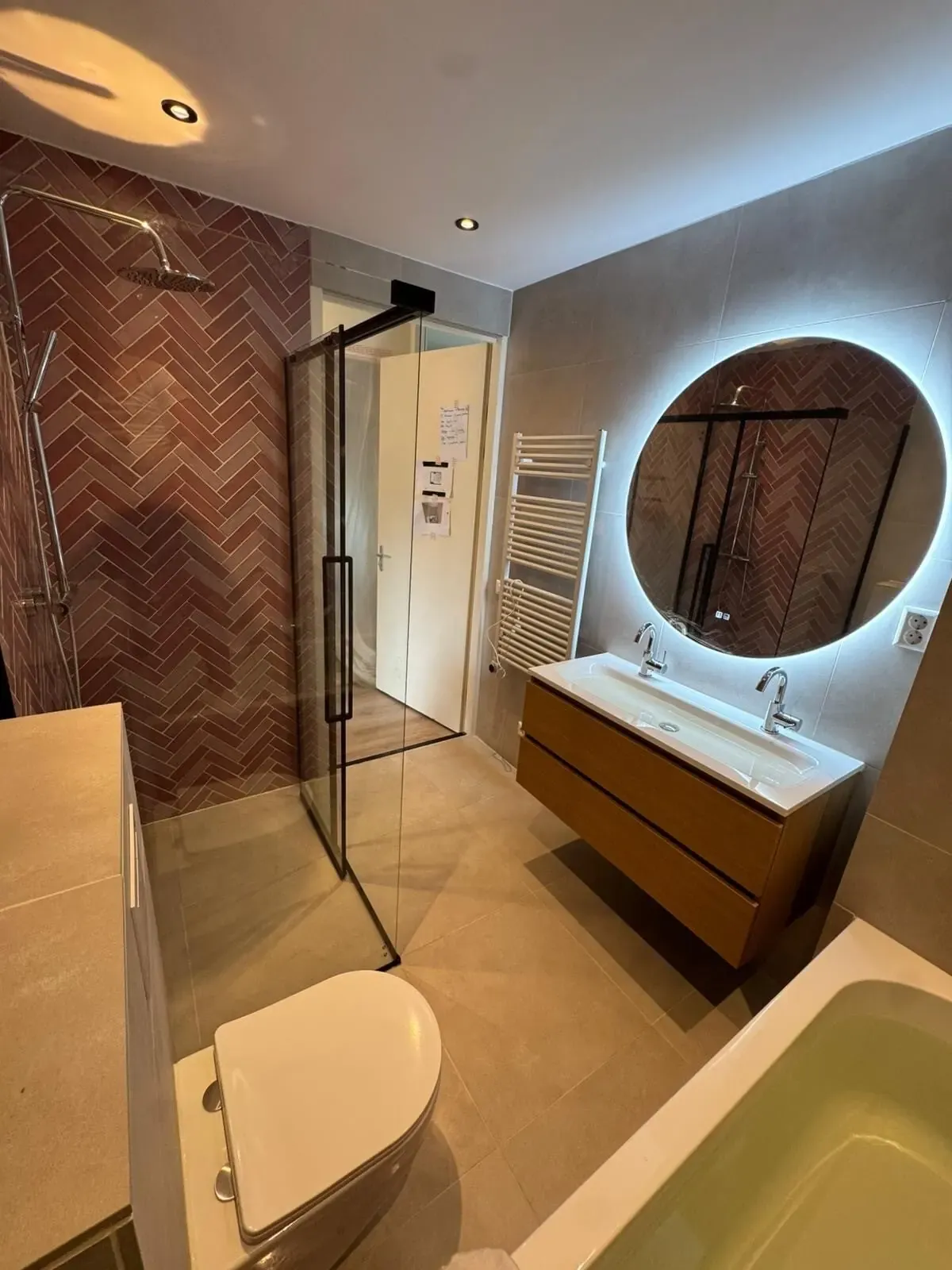 Badkamer met inloopdouche, terracotta visgraatwand en ronde ledspiegel