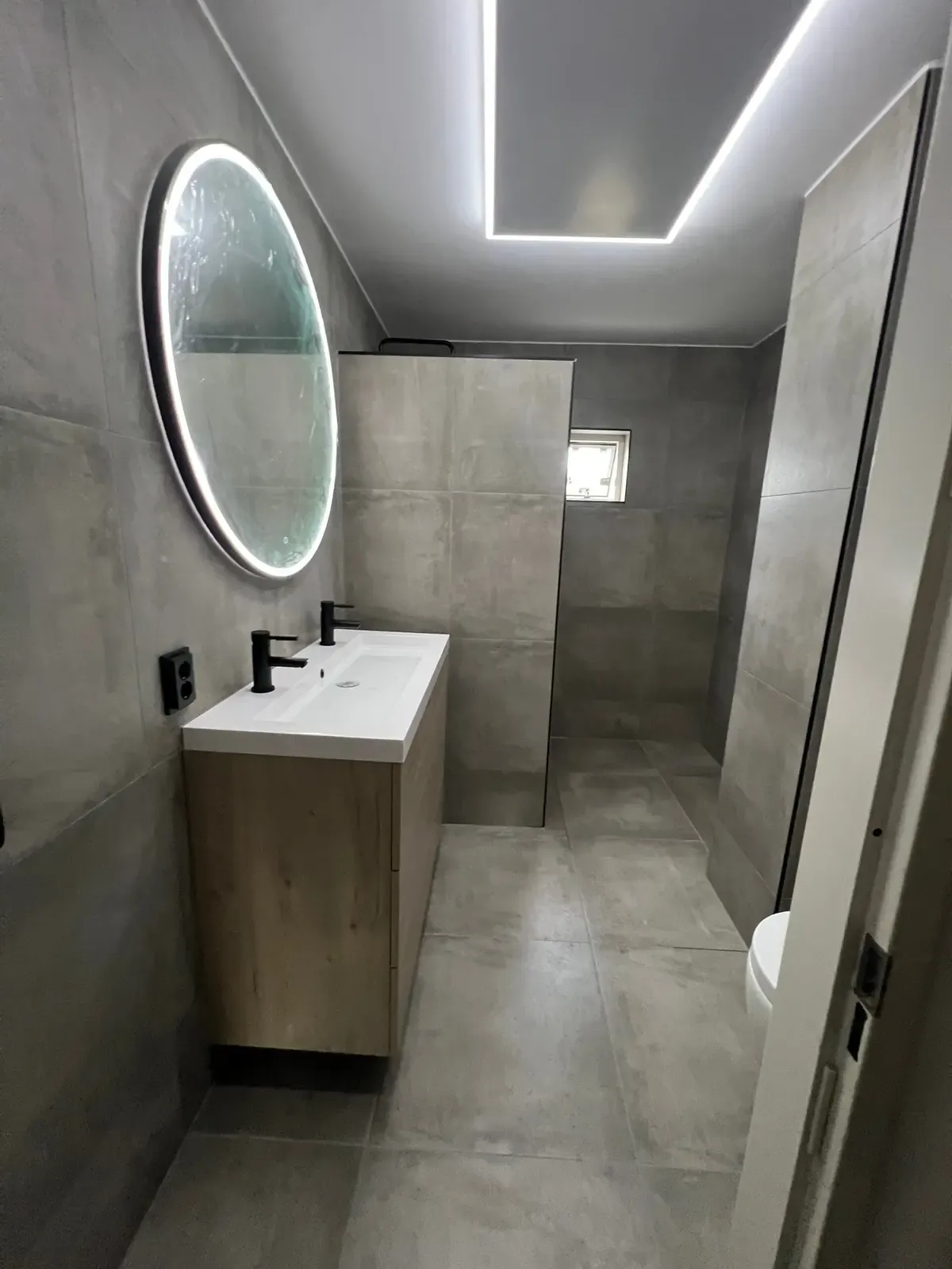 Badkamer met betonlooktegels, ronde ledspiegel en zwart kraanwerk