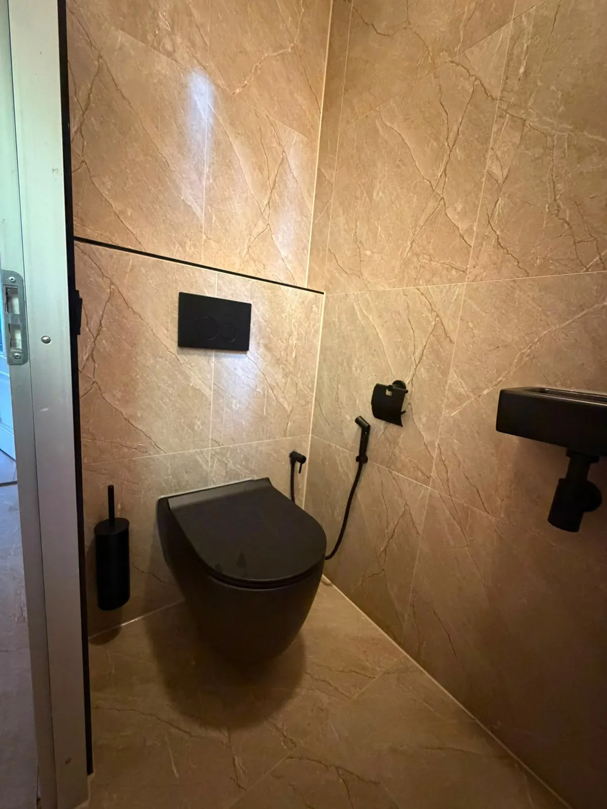 Toilet met warme marmerlook tegels, zwart hangtoilet en zwart fonteintje